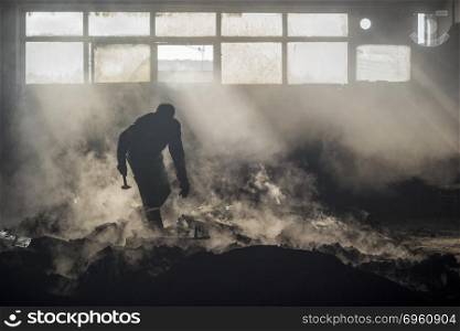 a foundry worker silhouette with his hammer,working environment with high temperature and fog