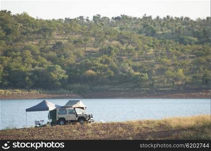 A four by four vehicle by the water with tents and fishing rods set up.