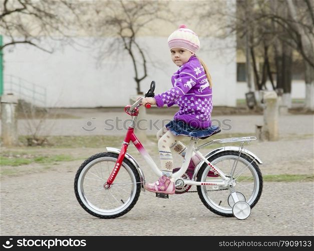 A four year old girl goes on a Bicycle on an asphalt-paved road. A warm spring day.
