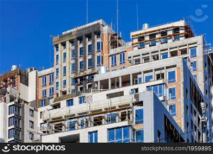 A fragment of the construction of a multi-storey residential building with facade insulation and finishing with metal-plastic panels. Blue sky background, copy space.. Modern construction of a high-rise residential building with the concept of insulation and facade decoration.