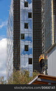 A fragment of the facade and insulation of a house under construction using a winch and a mobile platform, installation of large window frames, reconstruction of a residential building.. Reconstruction, facade insulation and installation of large windows in a modern residential building using a winch and a mobile platform.