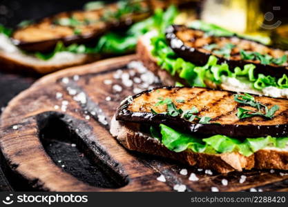 A fragrant sandwich with grilled eggplant on a cutting board. Against a dark background. High quality photo. A fragrant sandwich with grilled eggplant on a cutting board.