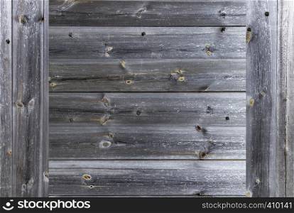 A frame in the form of a weathered old gray wooden fence, which is knocked down by wooden nails, close-up. A frame of a seasoned old gray wooden fence closeup
