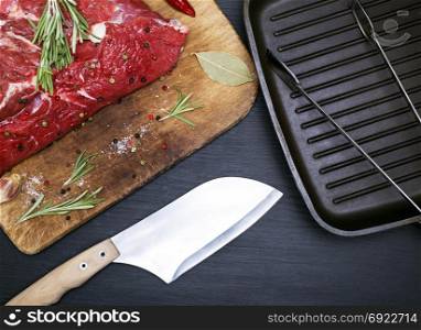 A fresh piece of beef on a kitchen cutting board and a black frying pan