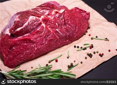 A fresh piece of beef on brown kraft paper with spices and a rosemary branch