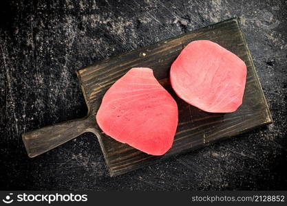 A fresh piece of raw tuna on a cutting board. On a black background. High quality photo. A fresh piece of raw tuna on a cutting board.