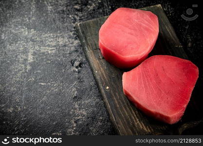 A fresh piece of raw tuna on a cutting board. On a black background. High quality photo. A fresh piece of raw tuna on a cutting board.