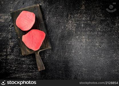 A fresh piece of raw tuna on a cutting board. On a black background. High quality photo. A fresh piece of raw tuna on a cutting board.