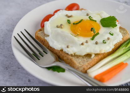 A fried egg laying on a toast, topped with pepper seeds with carrots and spring onions.