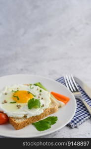 A fried egg laying on a toast, topped with pepper seeds with carrots and spring onions.