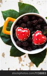 A full blackberry plate with a heart-shaped dessert stands on an old wooden background. valentine card. A full blackberry plate with heart-shaped dessert
