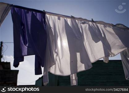 A full load of newly cleaned shirts are drying in the warm sun while hanging from a clothesline in a South African township.