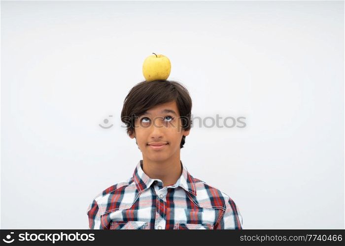 A funny portrait of a young attractive Arab boy with an apple on his head isolated on a white background. Selective focus. High quality photo. A funny portrait of a young attractive Arab boy with apple on his head isolated on a white background. Selective focus