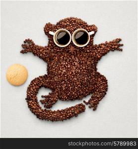 A funny tarsier made of roasted coffee beans, two cups and star anise with an oatmeal cookie.