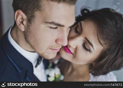 A gentle kiss of the newlyweds on the background of bright Windows.. The young husband and wife gently kiss each other on the background of bright Windows 6462.