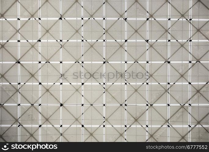 A geometric pattern of fabric squares is supported by a lattice structure of beams overhead in a museum. The cloth is dirty in sections.