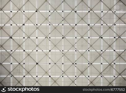 A geometric pattern of fabric squares is supported by a lattice structure of beams overhead in a museum. The cloth is dirty in sections.