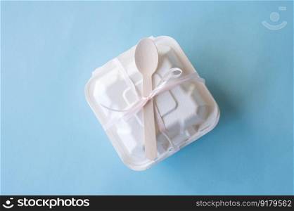 A gift box for a bento cake with a wooden spoon stands closed on a blue background. A bento cake with a wooden spoon is packed