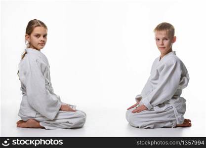 A girl and a boy in a sports kimono sit opposite each other and looked into the frame