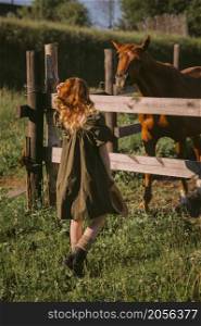 A girl and a paddock with horses.. A red-haired girl is standing near a paddock with horses 3234.