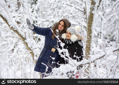 A girl and her daughter are walking through the snowy forest, the girl shows something interesting