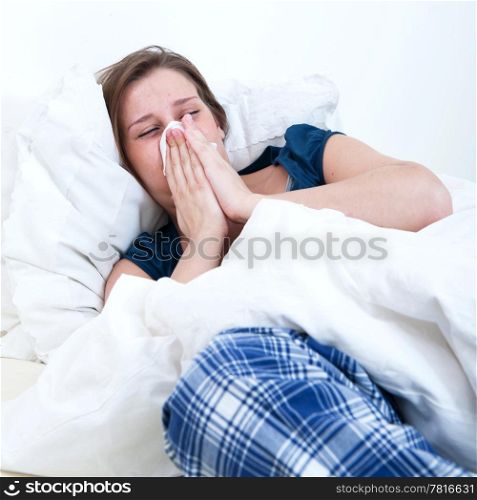 A girl blowing her nose while lying sick in bed.