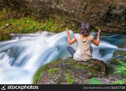 A girl doing yoga near the birth of a river from the rock