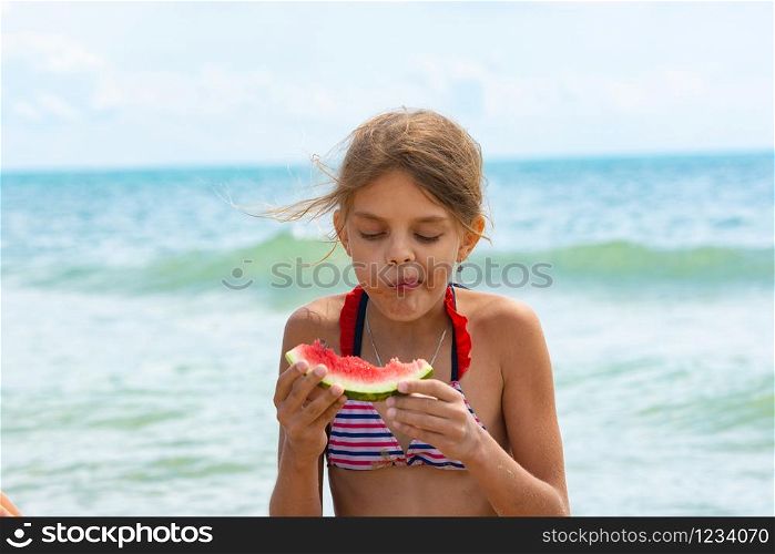A girl eats a watermelon on the beach