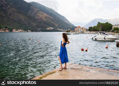 A girl in a blue dress stands on a pier near the Bay of Kotor, Montenegro. Nice and cozy city. A girl in a blue dress stands on a pier near the Bay of Kotor, Montenegro. Nice and cozy city.