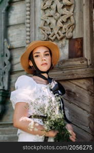 A girl in a hat and a white blouse walks against the background of old wooden houses.. A girls summer walk against the background of an ancient city 3574.