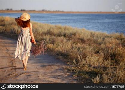 a girl in a hat and with a bouquet walks along the seashore