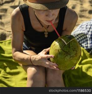 A girl in a hat drinks coconut juice through a straw.. A girl in a hat drinks coconut juice through a straw