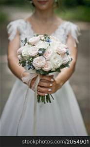 A girl in a wedding dress holds a bouquet at arms length.. A bouquet of roses in the hands of the bride 2756.
