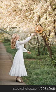 A girl in a white dress walks near a cherry blossom.. A joyful girl walks in the alley of flowering trees 2708.