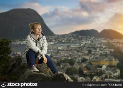 A girl in Alesund is sitting alone on a mountain. Norway