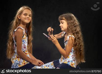 A girl is applying powder to a brush; another girl is looking into the frame with pleasure