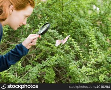 A girl looking at a butterfly with a magnifying glass