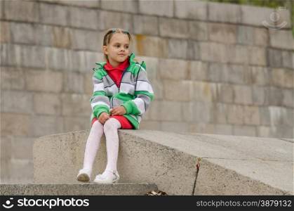 A girl of six years walking on the embankment. girl looks into distance while sitting a granite embankment on ramp