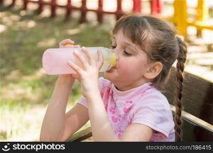 A girl on a bench on a hot day drinking water from a bottle
