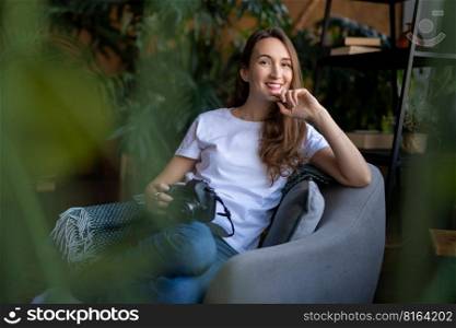 a girl photographer with a camera smiles while sitting in a chair with many books