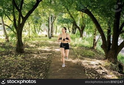A girl running in a park while listening to music. Lifestyle of beautiful girl running in a park surrounded by trees. Healthy lifestyle concept, Sporty young woman running in a park