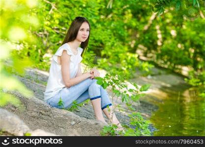 A girl sits on the concrete bank of the river. Cute girl Europeans sitting on the concrete bank of the river