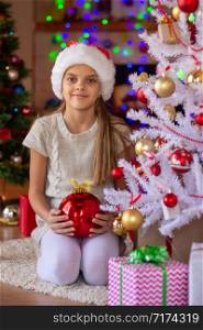 A girl sits with a red balloon at the Christmas tree