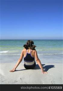 a girl sitting on the beach enjoying the sun