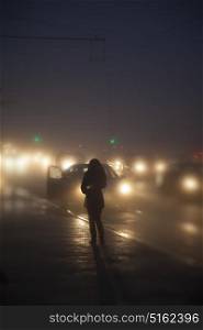 A girl stands near a road with cars at night