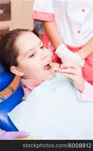A girl tries to establish a retainer for Teeth Dental Braces, sitting in a dental chair