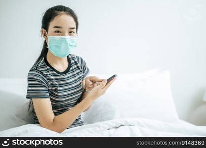A girl wearing a mask and a striped shirt playing a smartphone. Selective focus.