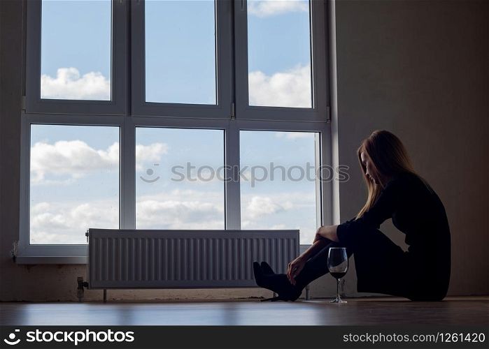 A girl with a glass of wine sits on the floor at a large stained glass window