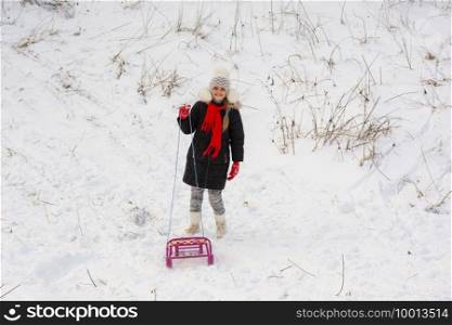A girl with a sled stands in a snowy meadow