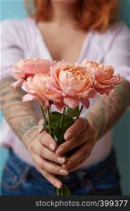 A girl with a tattoo holds a beautiful bouquet of pink roses around a blue background with copy space. Mother's Day Gift. A woman with a tattoo holding delicate pink roses in her hands on a blue background with copy space for text. Holiday gift